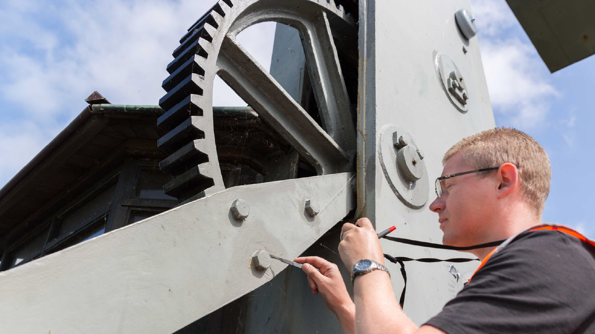 RPS medewerker schraapt oude verf van een groot metalen kunstwerk voor Chroom VI onderzoek.